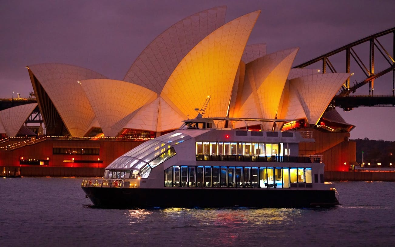 Glass boat dinner cruise with Sydney Opera House illuminated in the background.