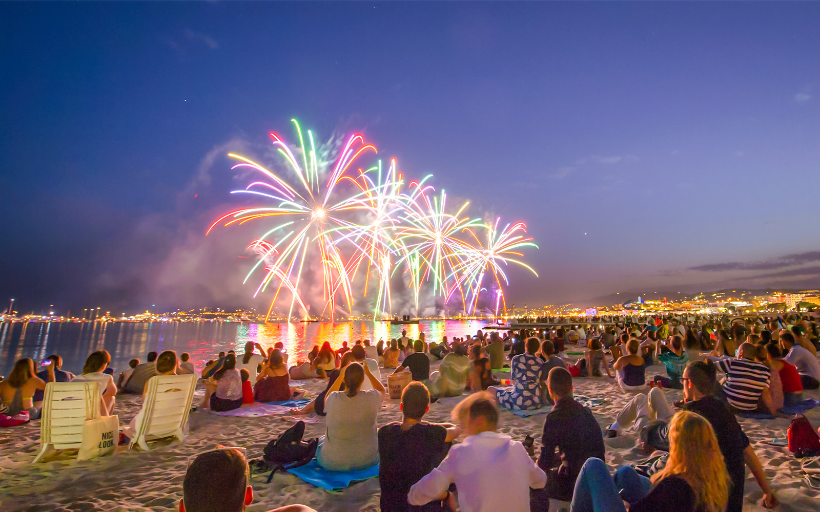Crowd watching Bastille Day fireworks over a beach in the evening.