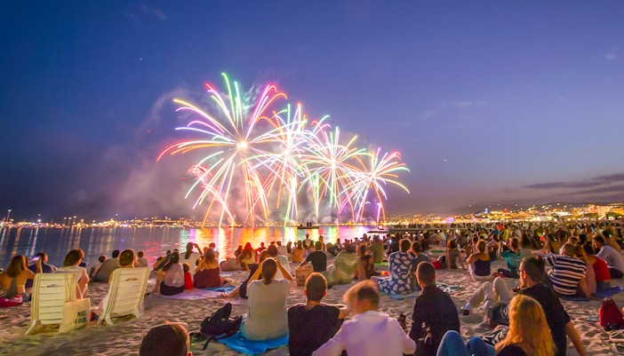 Crowd watching Bastille Day fireworks over a beach in the evening.