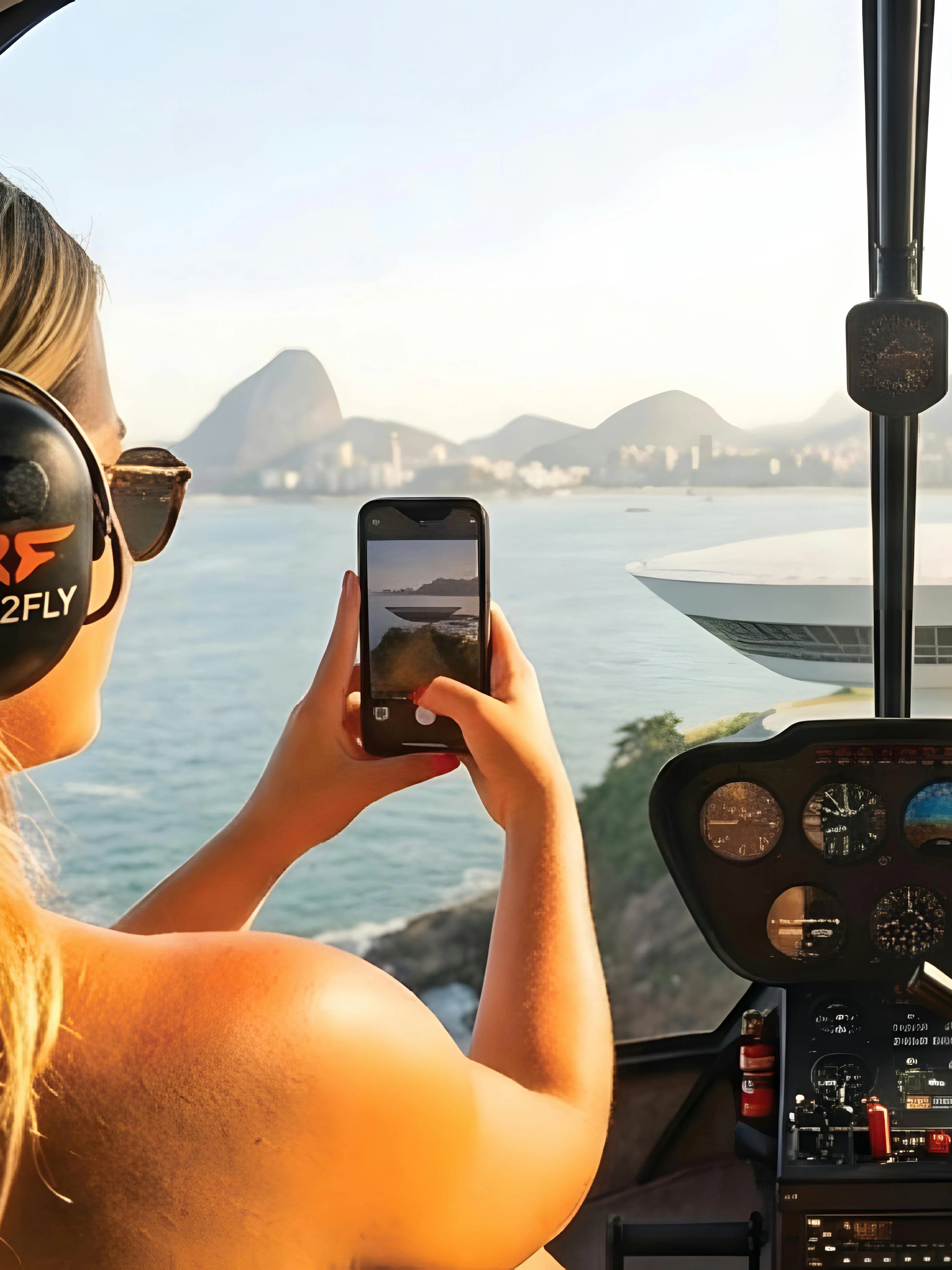 Tourist capturing Rio de Janeiro skyline from helicopter with Sugarloaf Mountain view.