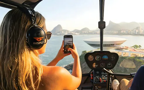 Tourist capturing Rio de Janeiro skyline from helicopter with Sugarloaf Mountain view.
