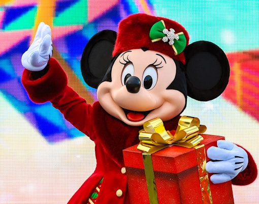 Character in festive attire holding a Christmas gift at Disneyland Paris.