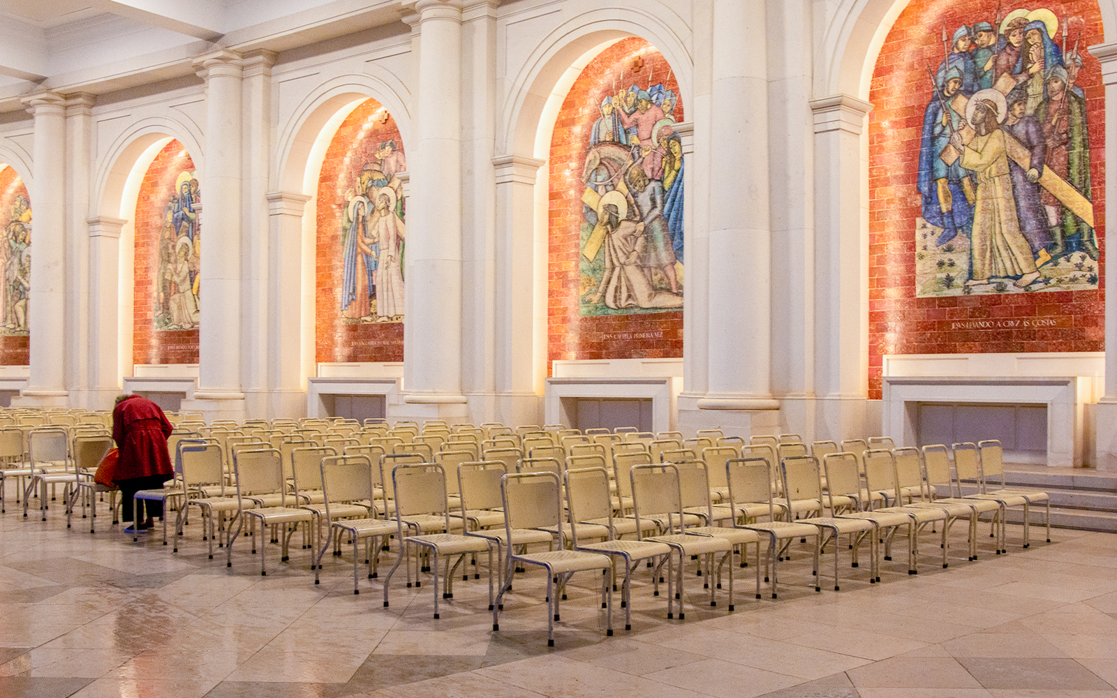 Rows of chairs inside the Sanctuary of Fatima, Portugal, with religious murals on the walls.