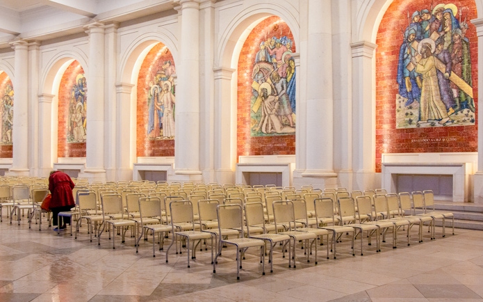 Rows of chairs inside the Sanctuary of Fatima, Portugal, with religious murals on the walls.