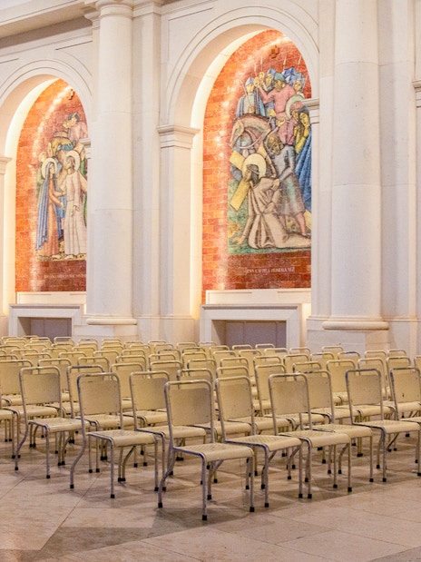 Rows of chairs inside the Sanctuary of Fatima, Portugal, with religious murals on the walls.