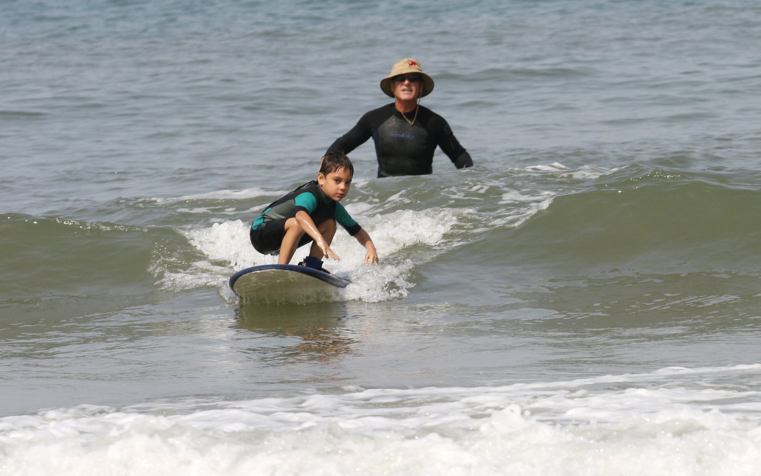 Instructor guiding child on surfboard during surf class in Lisbon.
