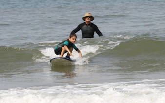 Instructor guiding child on surfboard during surf class in Lisbon.