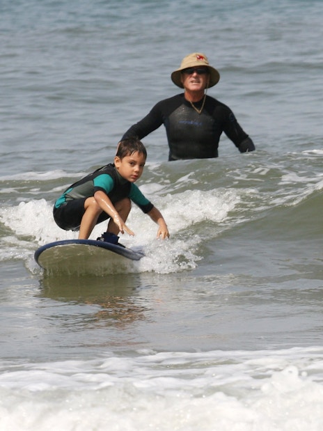 Instructor guiding child on surfboard during surf class in Lisbon.