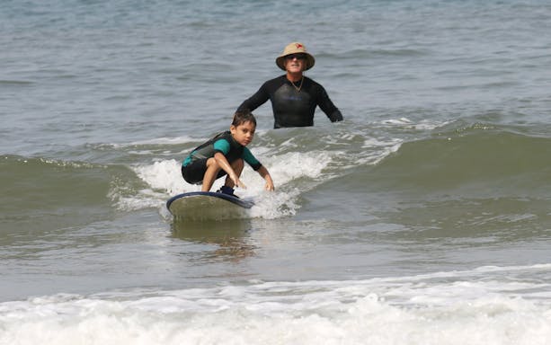 Instructor guiding child on surfboard during surf class in Lisbon.