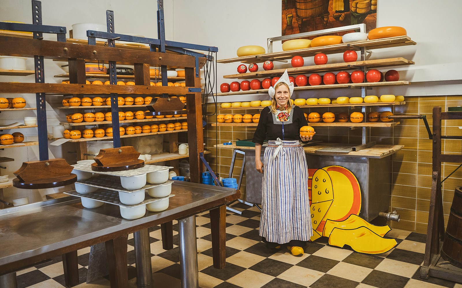 Woman in traditional attire holding cheese at a Dutch cheese farm and clog factory.