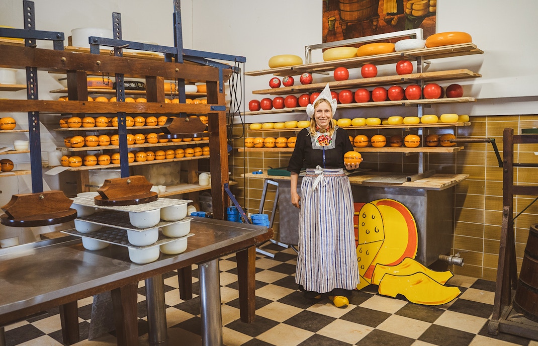 Woman in traditional attire holding cheese at a Dutch cheese farm and clog factory.