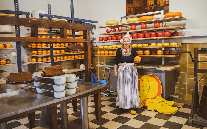 Woman in traditional attire holding cheese at a Dutch cheese farm and clog factory.