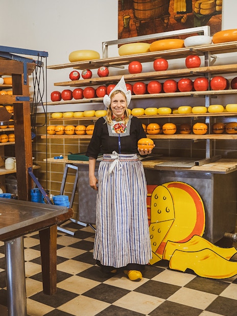 Woman in traditional attire holding cheese at a Dutch cheese farm and clog factory.
