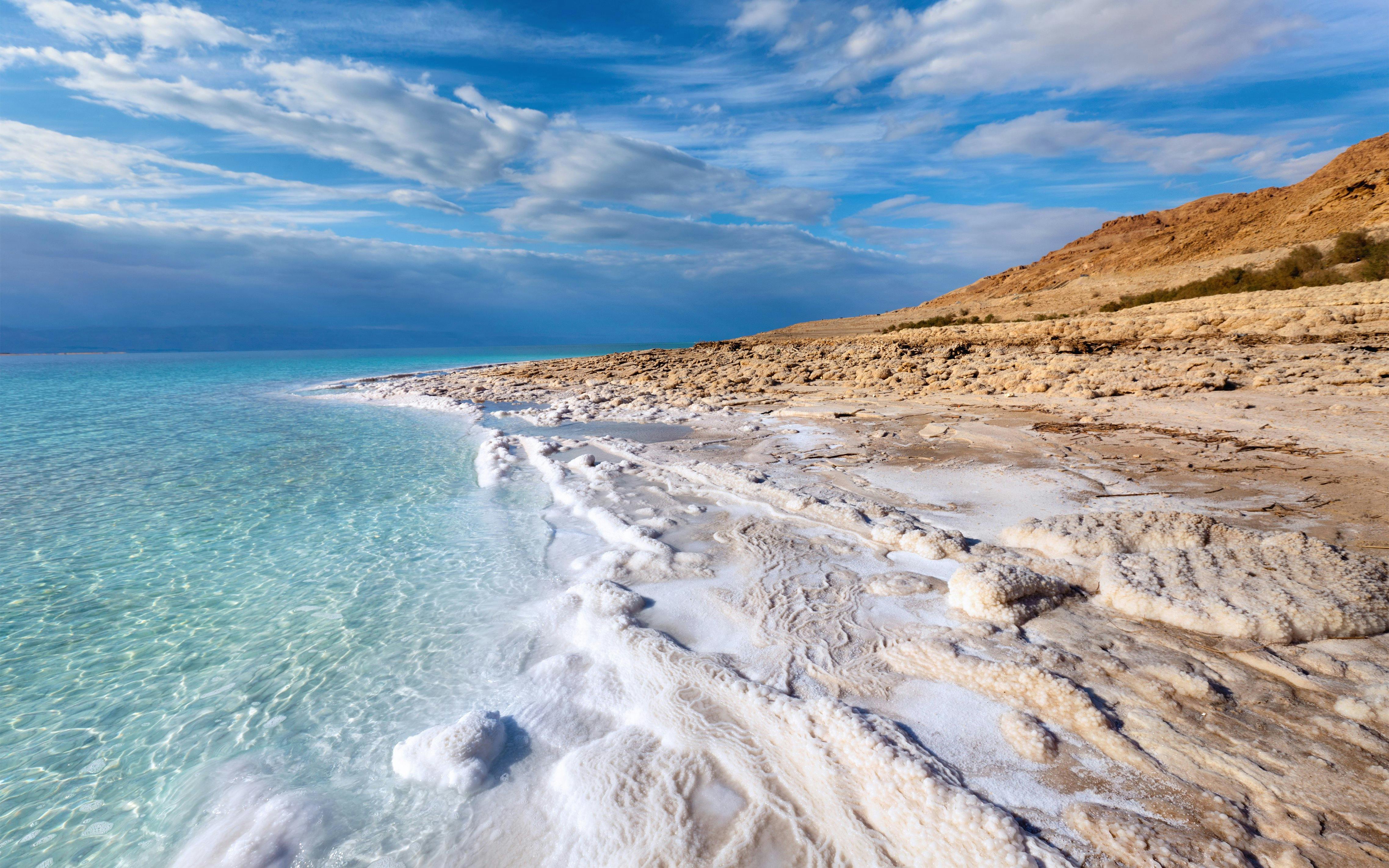 Dead Sea coastline with salt formations and clear blue water.