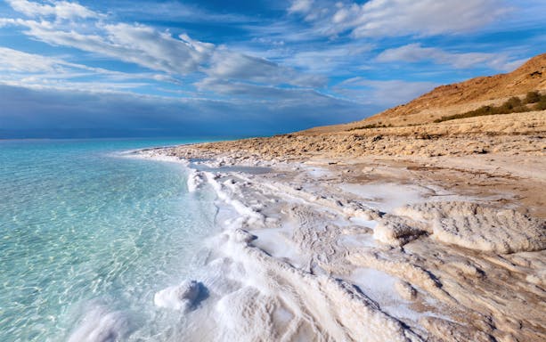 Dead Sea coastline with salt formations and clear blue water.