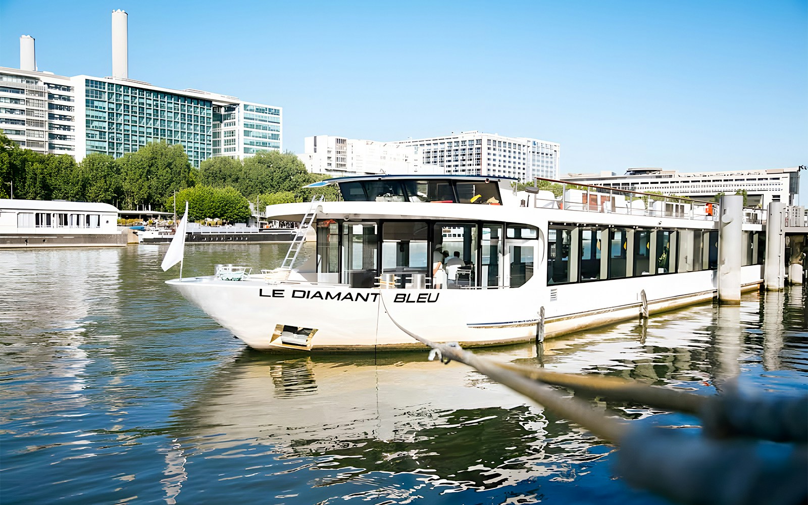 Seine River cruise boat with dining setup, Paris landmarks in background, Le Diamant Bleu Gourmet Dinner.