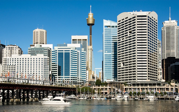 Sydney Tower rising above city skyline with boats in Darling Harbour.