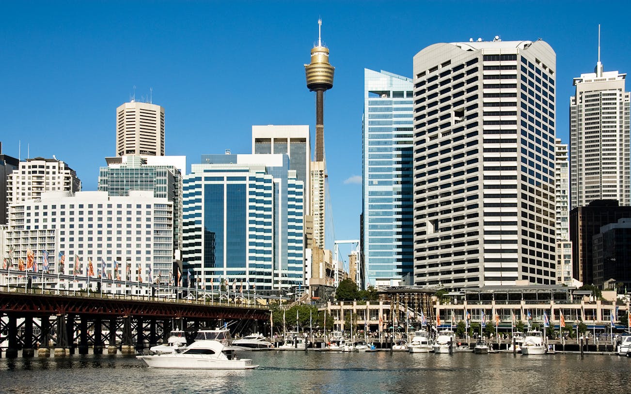 Sydney Tower rising above city skyline with boats in Darling Harbour.