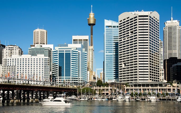 Sydney Tower rising above city skyline with boats in Darling Harbour.