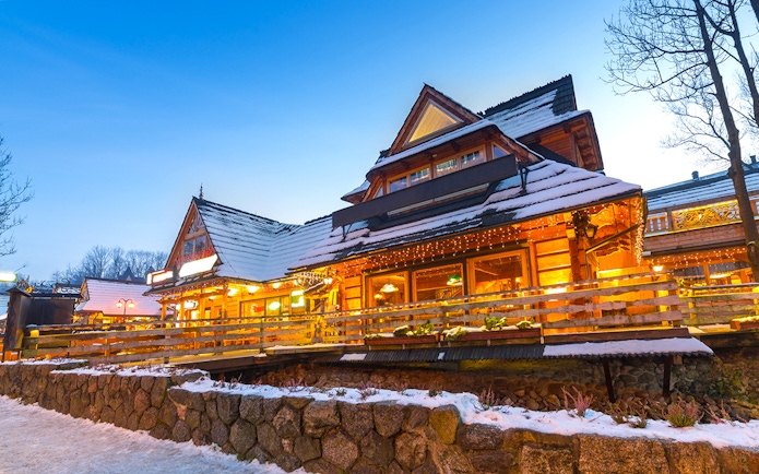 Wooden chalet in Zakopane with snow-covered roof and warm lights at dusk.