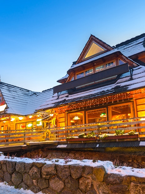 Wooden chalet in Zakopane with snow-covered roof and warm lights at dusk.
