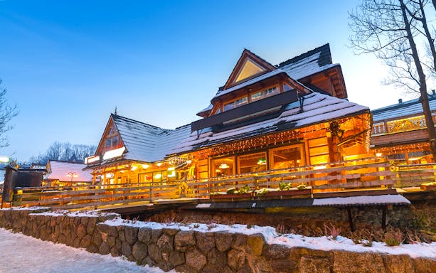 Wooden chalet in Zakopane with snow-covered roof and warm lights at dusk.