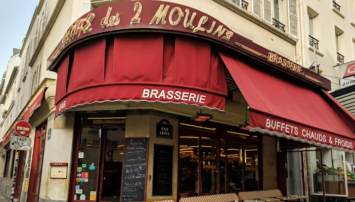 Couple walking past Café des 2 Moulins in Montmartre, Paris.