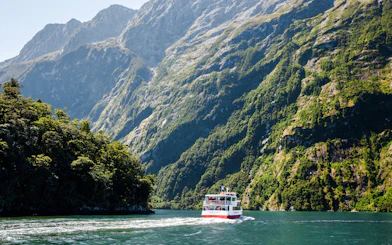 Cruise boat navigating Milford Sound fjord with lush mountains, Te Anau tour.