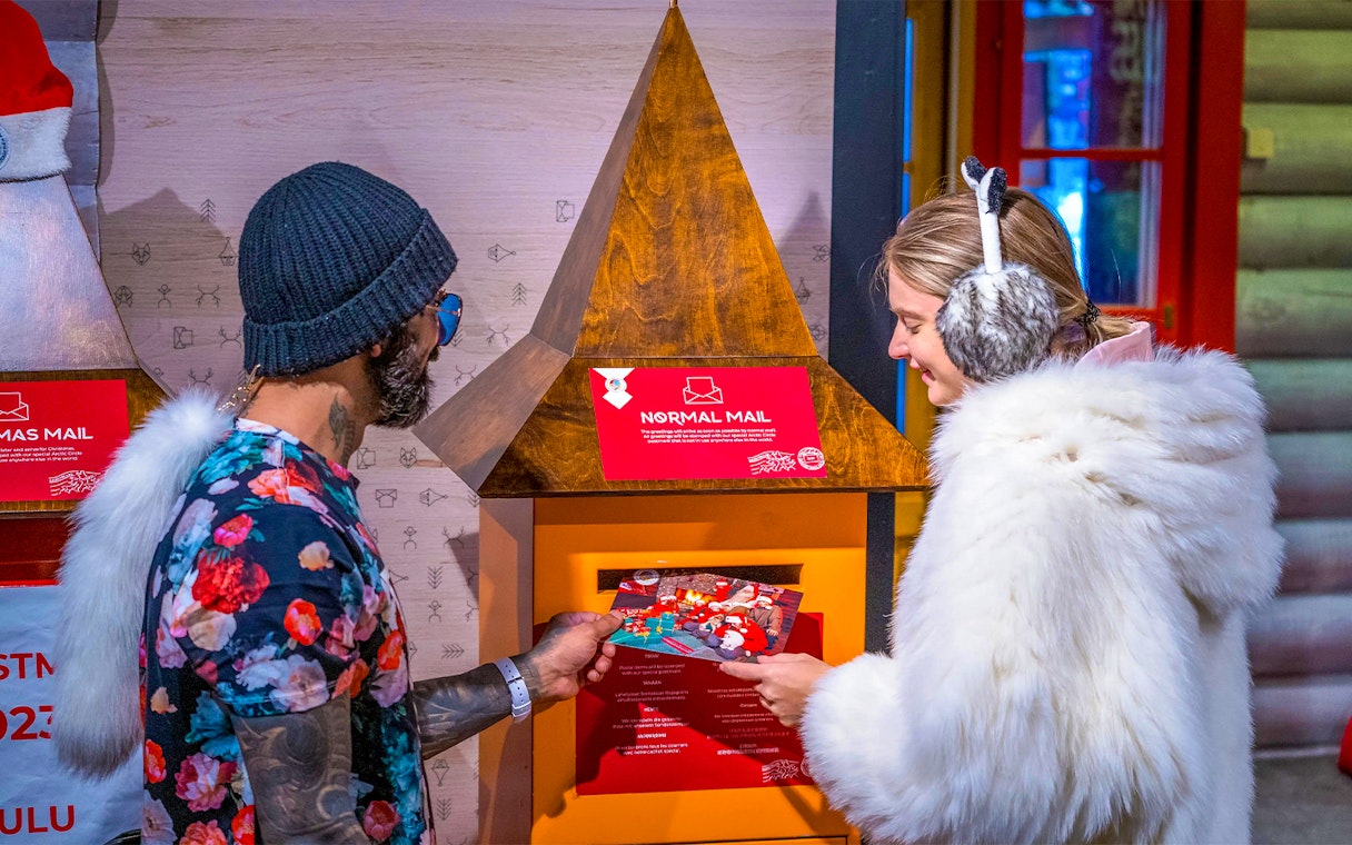 Guests at Santa Claus Village Rovaniemi sending postcards in festive setting.