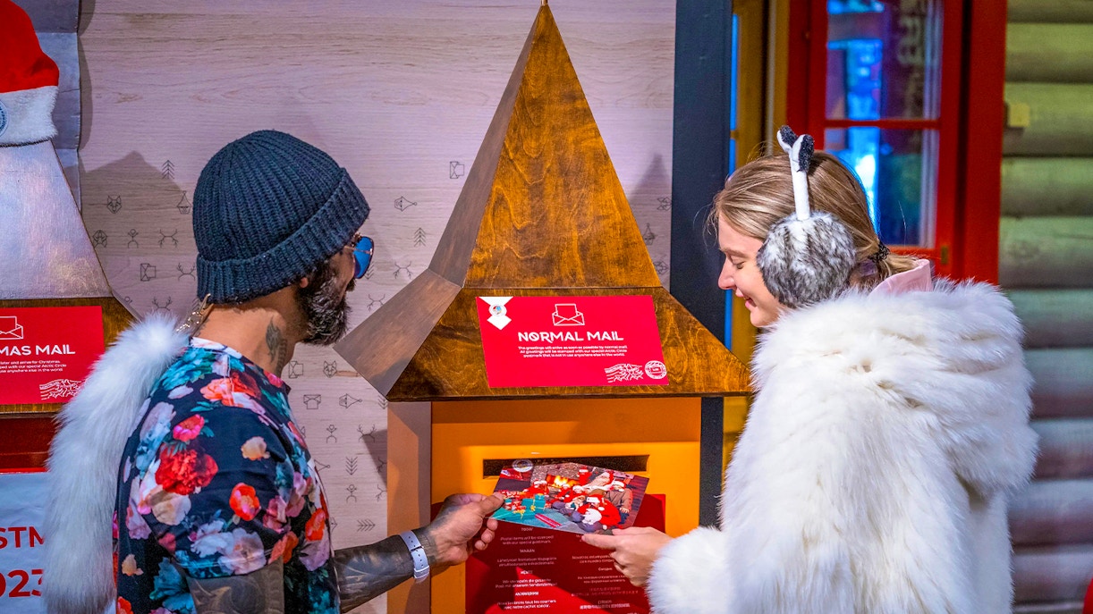 Guests at Santa Claus Village Rovaniemi sending postcards in festive setting.