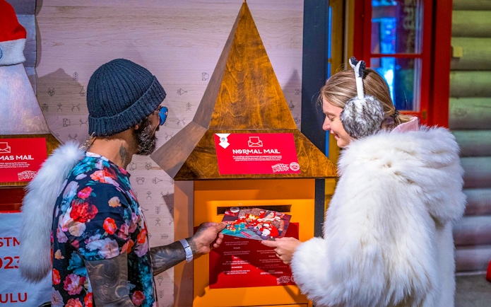Guests at Santa Claus Village Rovaniemi sending postcards in festive setting.