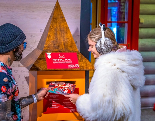 Guests at Santa Claus Village Rovaniemi sending postcards in festive setting.