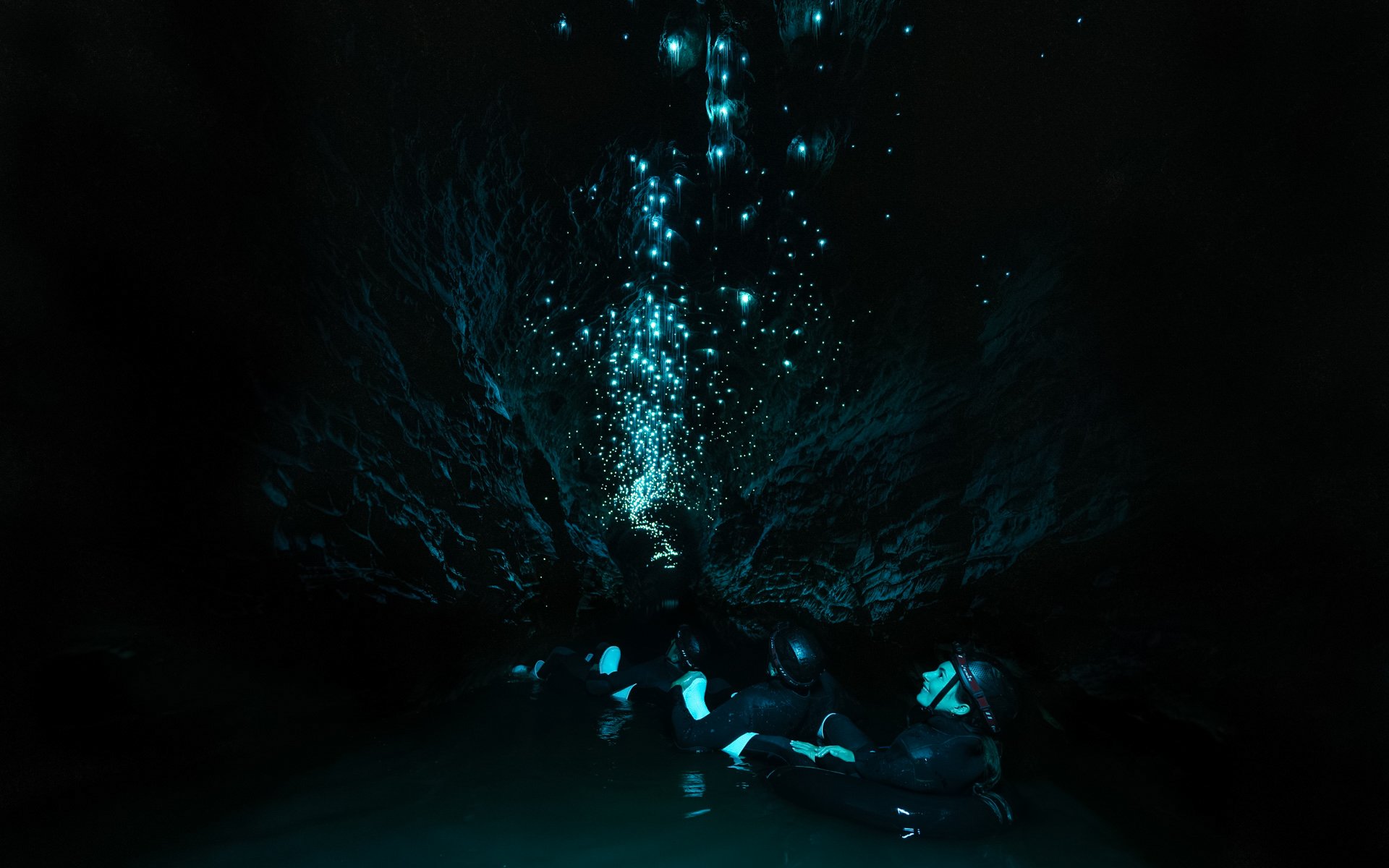Visitors floating in Okohua Glowworm Cave, illuminated by glowworms, Waitomo Experience.