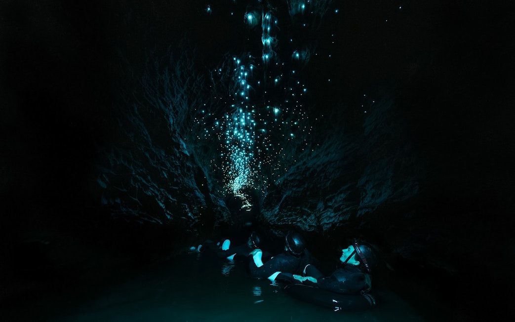 Visitors floating in Okohua Glowworm Cave, illuminated by glowworms, Waitomo Experience.