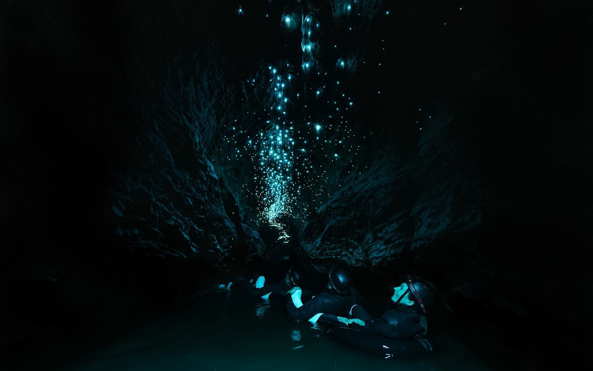 Visitors floating in Okohua Glowworm Cave, illuminated by glowworms, Waitomo Experience.
