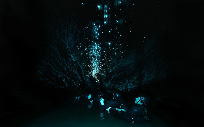 Visitors floating in Okohua Glowworm Cave, illuminated by glowworms, Waitomo Experience.