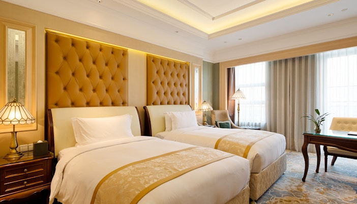 Hotel room with a bed, desk, and window in a generic setting.