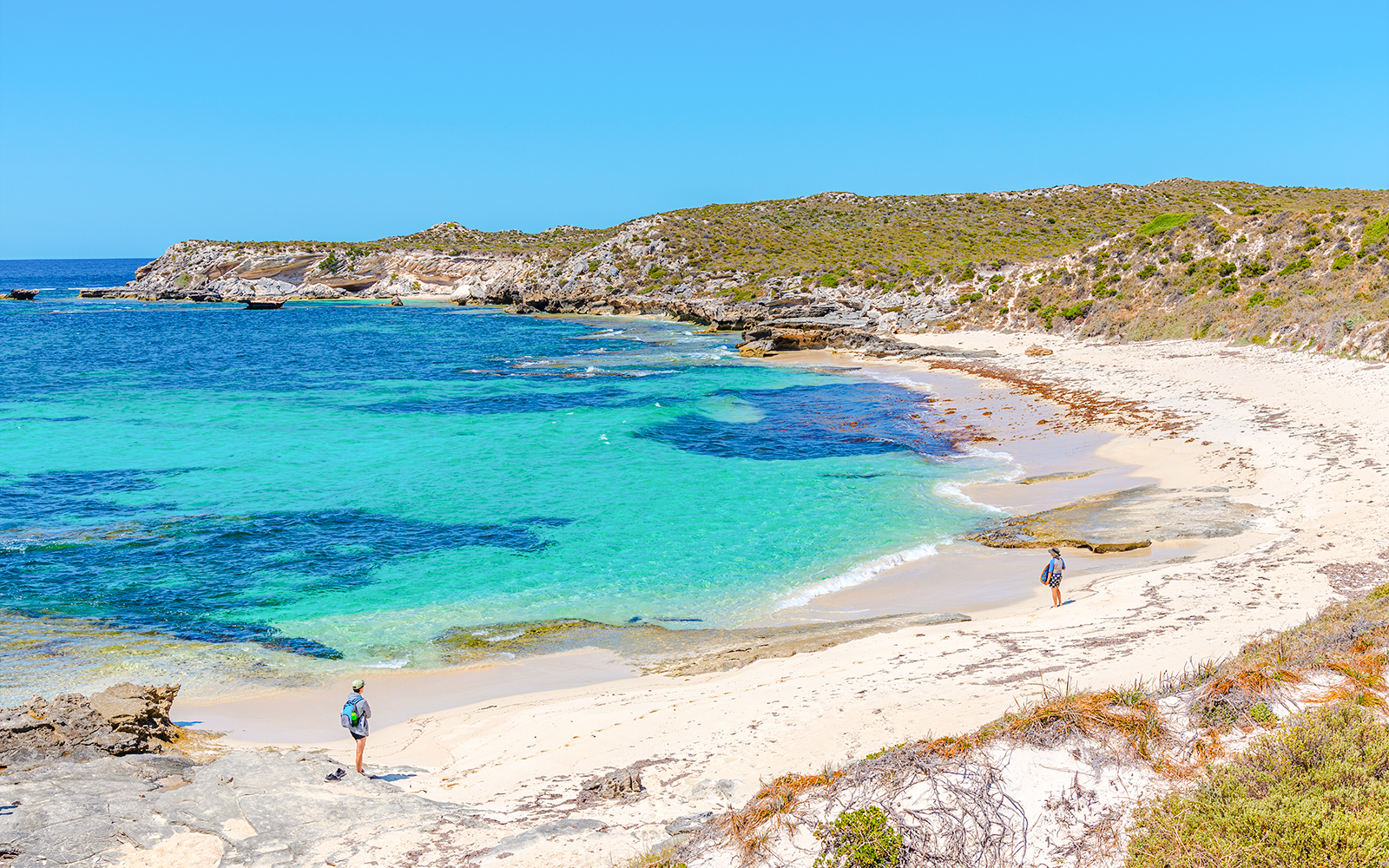 Visitors walking along the sandy shore of Strickland Bay, Rottnest Island, with clear turquoise water.