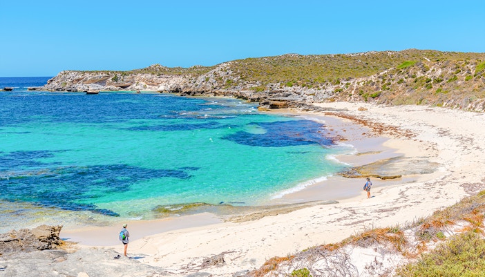 Visitors walking along the sandy shore of Strickland Bay, Rottnest Island, with clear turquoise water.