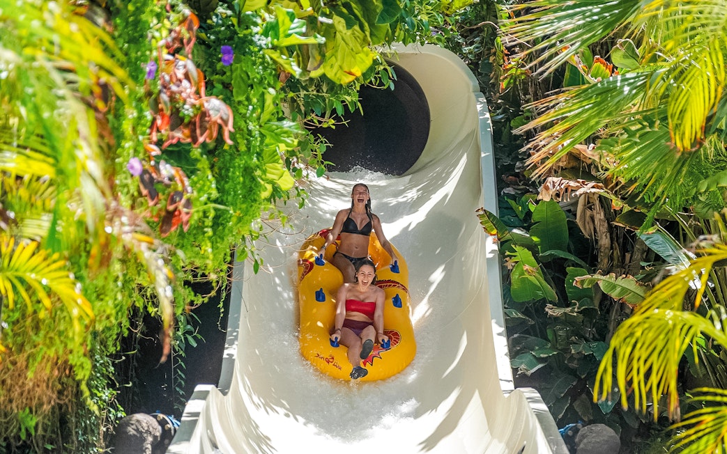Visitors enjoying a water slide at Siam Park, surrounded by lush greenery.