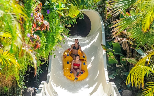 Visitors enjoying a water slide at Siam Park, surrounded by lush greenery.