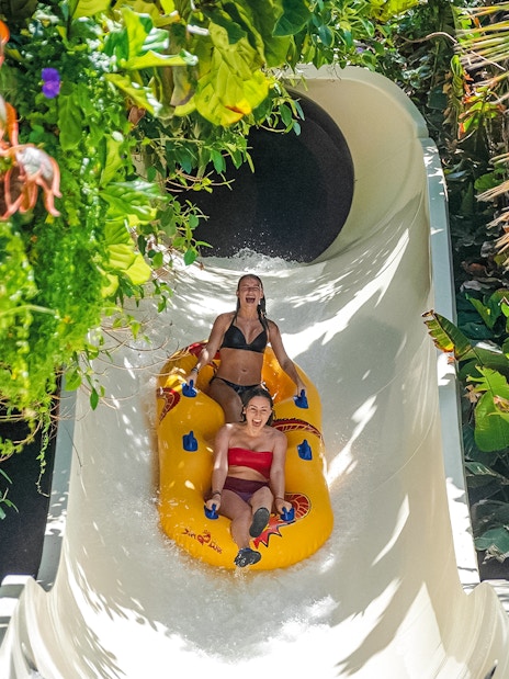 Visitors enjoying a water slide at Siam Park, surrounded by lush greenery.