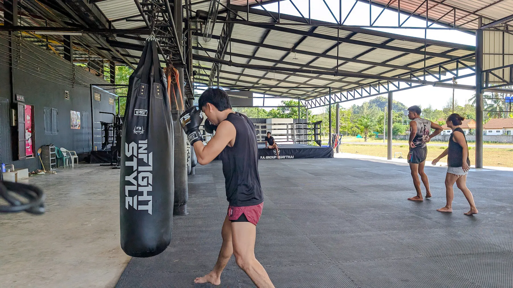 Muay Thai beginner practicing with punching bag in open-air gym, Ao Nang, Krabi.