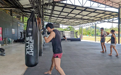 Muay Thai beginner practicing with punching bag in open-air gym, Ao Nang, Krabi.
