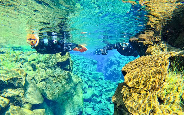 Snorkelers exploring clear waters and rock formations in Silfra, Iceland.