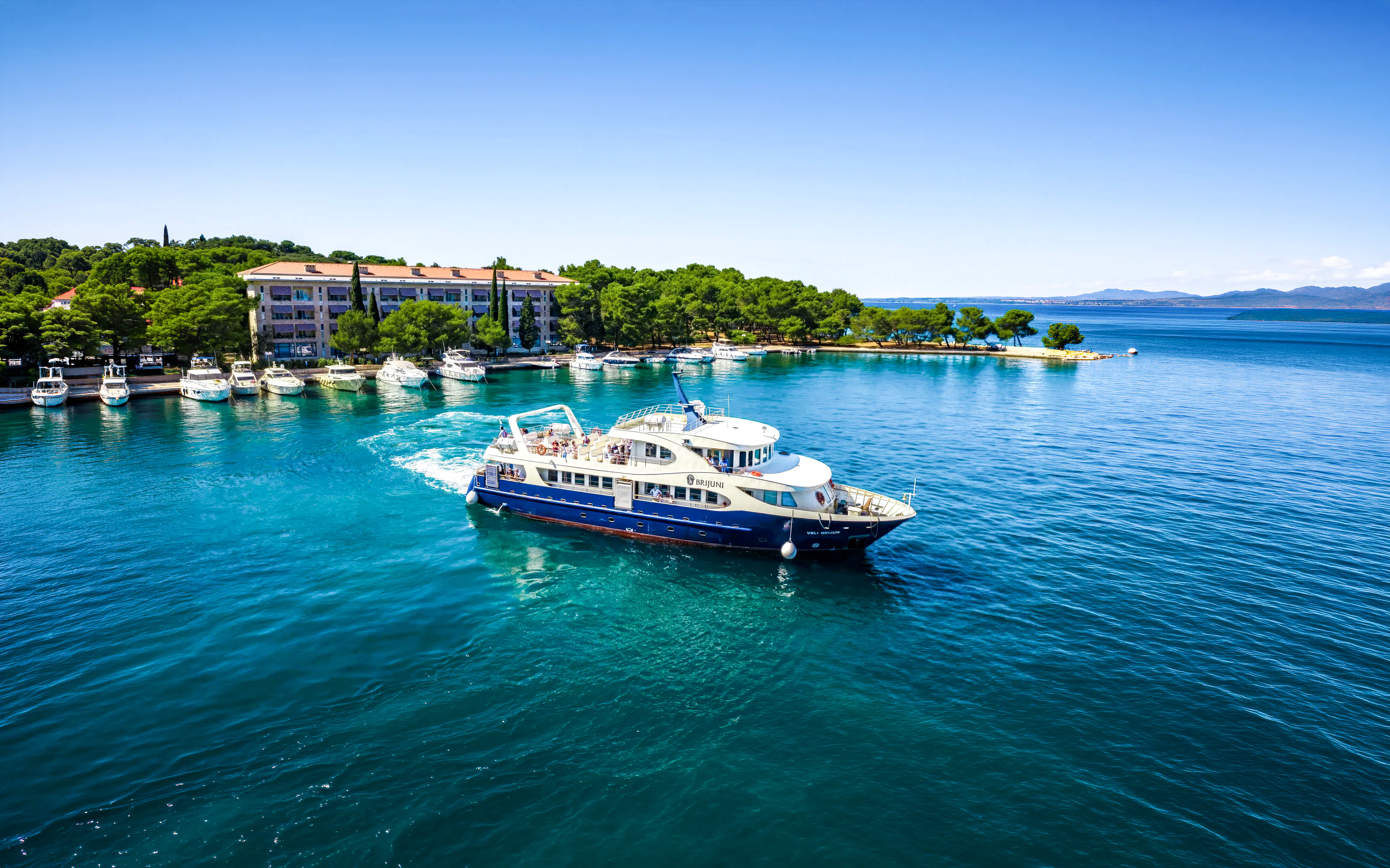 Boat cruising near Brijuni National Park with coastal buildings and trees in Fažana, Croatia.