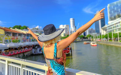 Boat cruising on Singapore River with city skyline and historic bridges in view.