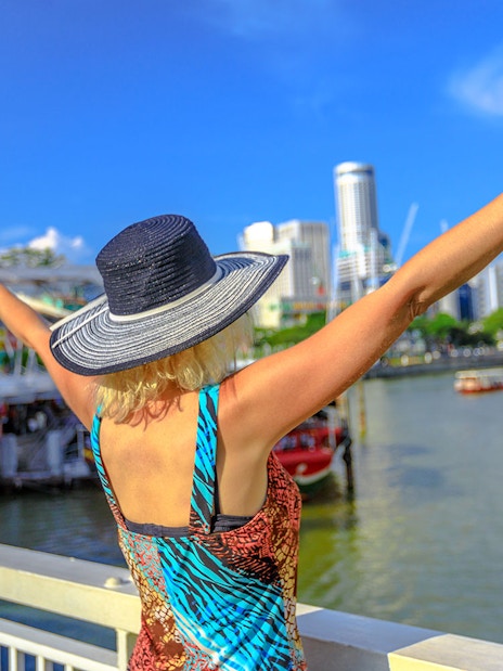 Boat cruising on Singapore River with city skyline and historic bridges in view.