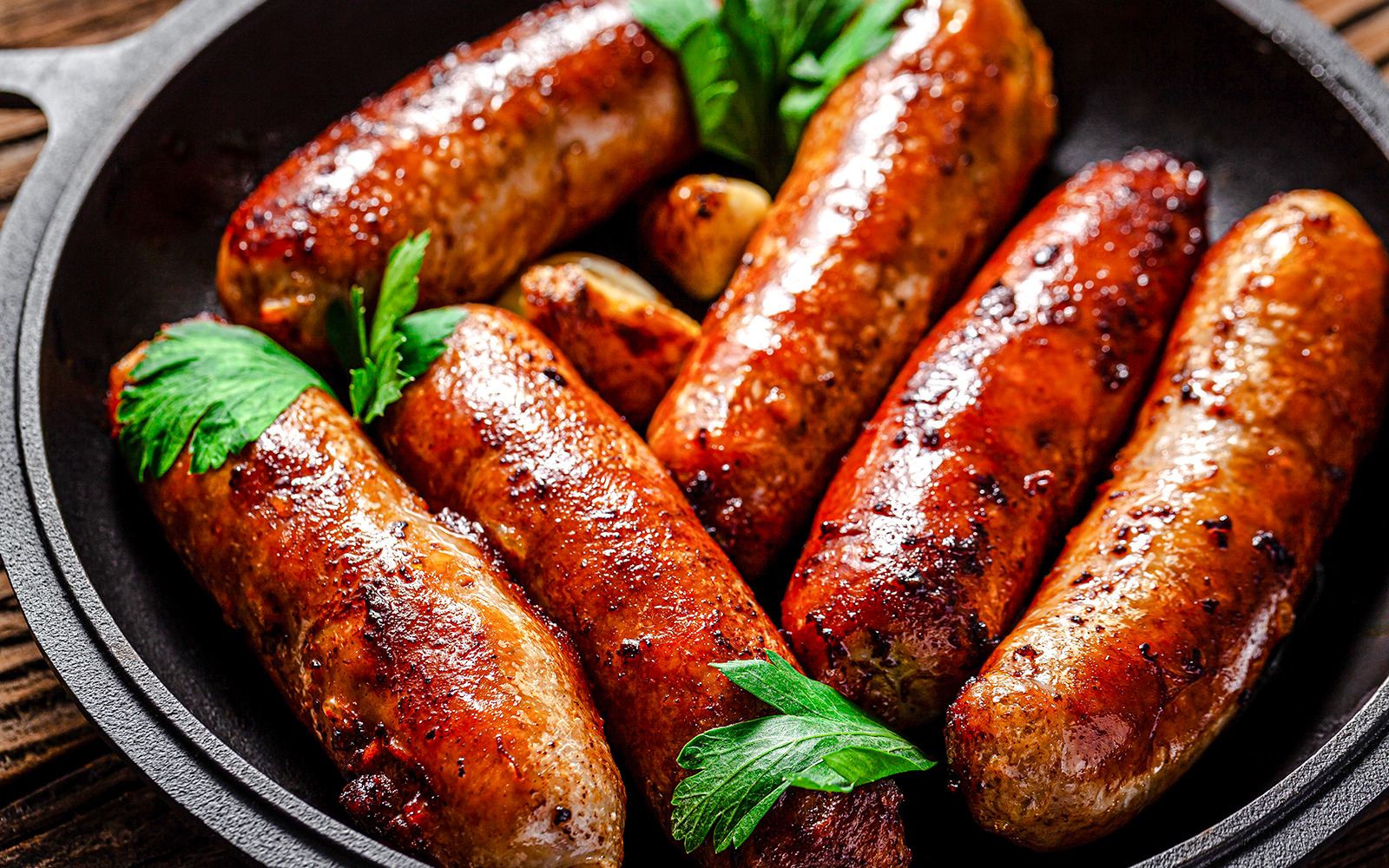 Sizzling sausages in a pan with parsley garnish, London food tour.