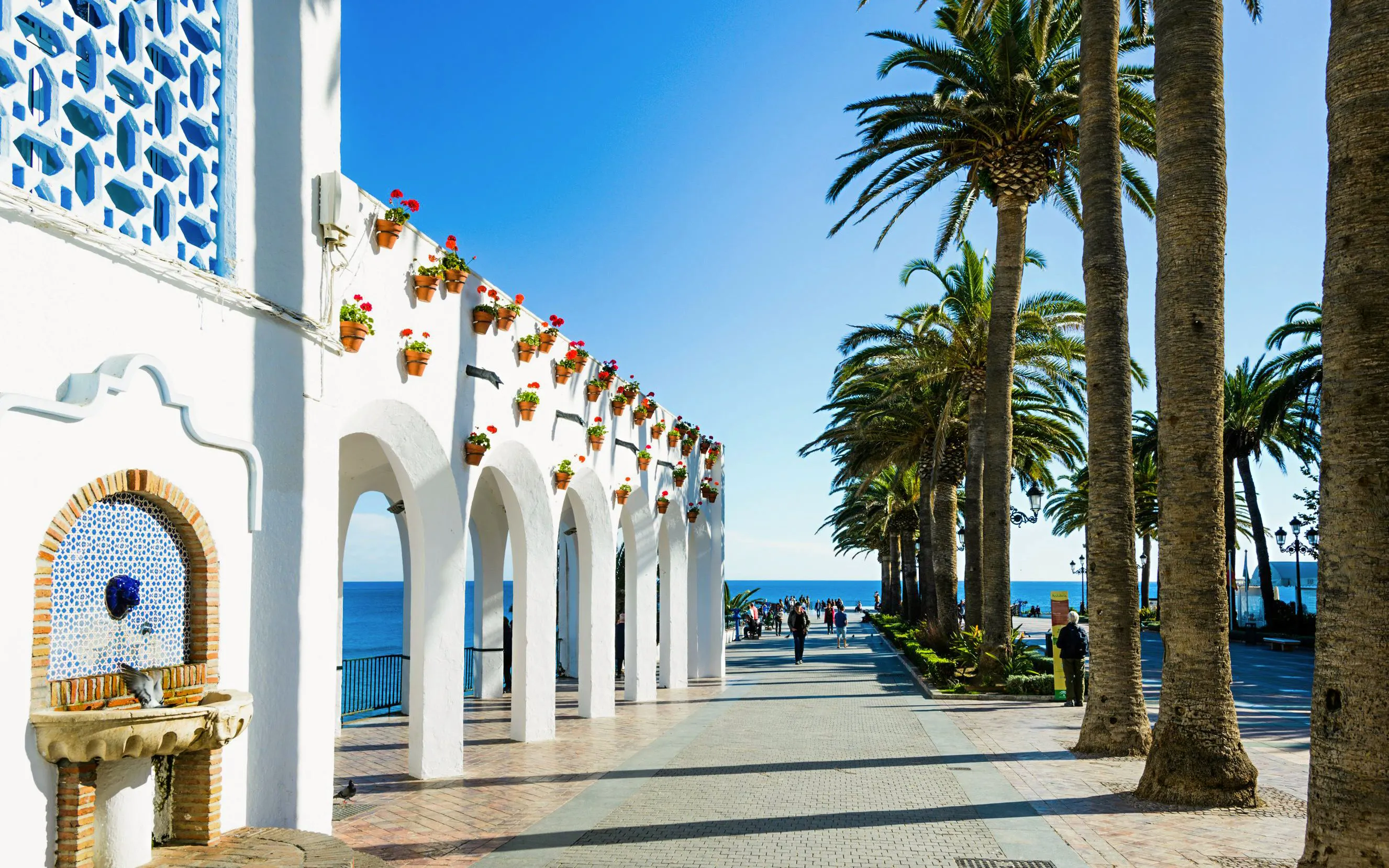 White arches and palm trees along the promenade at Plaza Balcon de Europa, Nerja, Spain.
